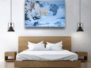 A polar bear mother stands on colorful snow-swept coastal rock ledges with her cub close, against a backdrop of exposed rock and winter light near Hudson Bay.